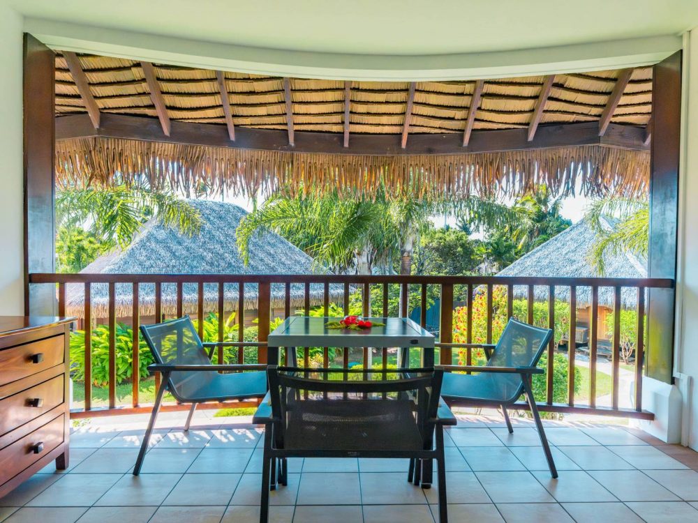 Furnished balcony of the Family Garden Duplex at Manava Beach Resort Moorea with a table, two chairs, and a view of the tropical garden.