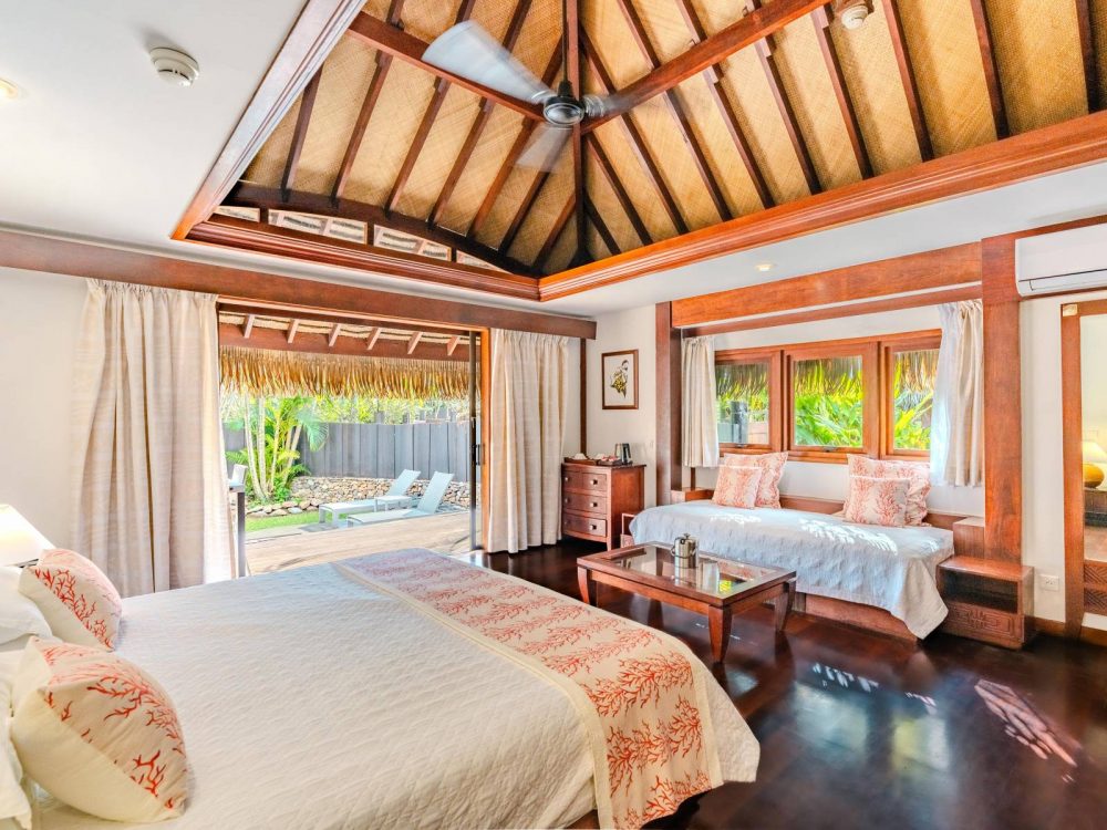 Interior of a Garden Bungalow at Manava Beach Resort Moorea featuring a king bed, Polynesian decor, and a view of the private outdoor pool.